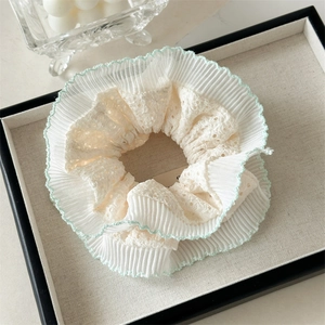 Détail du chouchou en dentelle crème avec broderie vert menthe et texture plissée fine