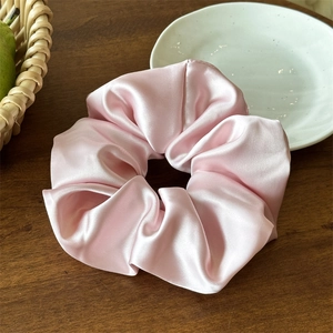 Dettaglio dell'elastico in raso rosa con texture setosa e pieghe su superficie in legno