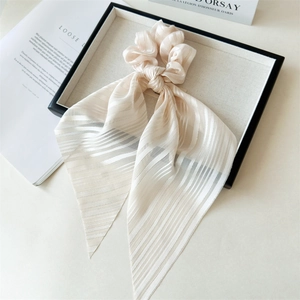 Détail du chouchou élégant beige à long ruban avec texture à rayures verticales et nœud