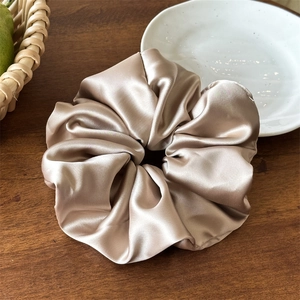 Dettaglio ravvicinato di elastico scrunchie in raso champagne con texture di seta e pieghe