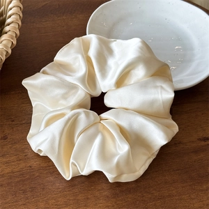 Dettaglio di un grande scrunchie in raso crema con finitura setosa e lucentezza morbida