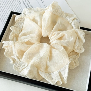 Detailed close-up of a creamy beige lace scrunchie with crochet trim texture
