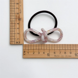 Détail d'un chouchou français avec nœud en acétate rose marbré et règle de mesure