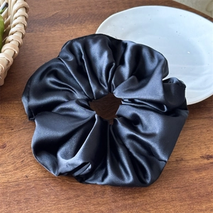Dettaglio dell'elastico in raso nero con trama in seta su fondo in legno scuro