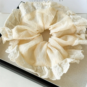 Detail view of cream fabric scrunchie with delicate white lace edges and soft pleats