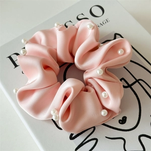 Détail d'un chouchou en satin rose clair avec perles blanches sur fond de livre épuré