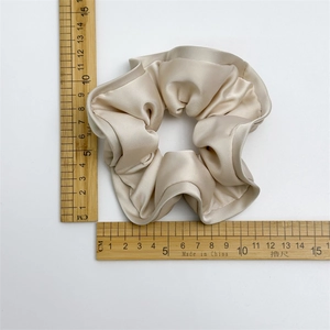 Elegant champagne satin scrunchie with large ruffles and soft silk texture on white background
