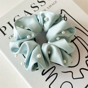 Détail d'un chouchou en satin bleu ciel orné de perles blanches avec texture soyeuse