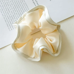 Close-up of cream satin scrunchie showing smooth fabric texture and ruffle edges