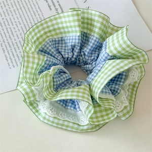 Détail d'un chouchou à carreaux verts et bleus avec bordure en dentelle blanche et tissu coton
