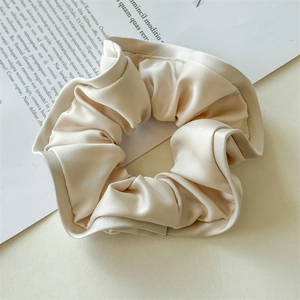 Detailed close-up of cream satin scrunchie with elegant ruffled texture on prop paper