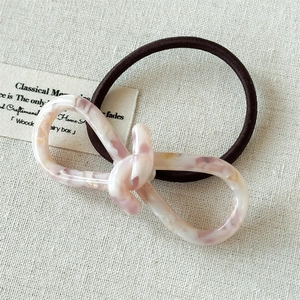 Détail d'un élastique à cheveux en résine marbrée avec élastique brun sur fond lin beige