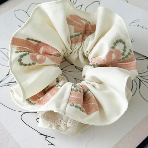 Close-up of pink bow embroidery and delicate lace trim on a creamy scrunchie