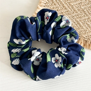 Gros plan d'un chouchou en mousseline fleurie bleu marine sur fond de bois et de jute