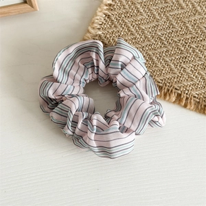 Détail d'un chouchou en mousseline rayée aux motifs rose pastel et gris sur bois clair