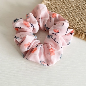 Détail d'un chouchou en mousseline rose clair avec des motifs floraux orange