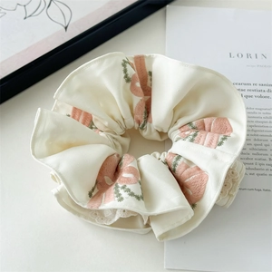 Off-white satin scrunchie with pink bow embroidery and lace trim on white tabletop