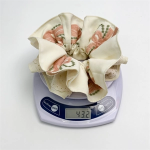 Detail shot of white lace scrunchie with pink bow embroidery on scale weighing 43.2g