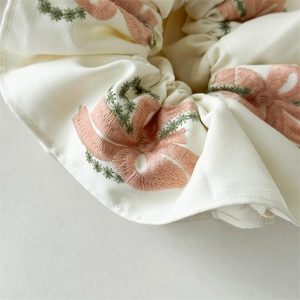 Detailed close-up of cream scrunchie with pink bow embroidery and floral leaf patterns