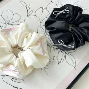 Close-up of satin scrunchies with bow embroidery detail in black and cream white