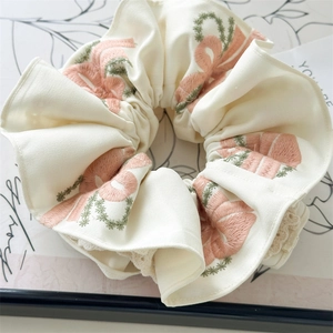 Close-up of beige embroidery scrunchie with floral pattern and white lace edge