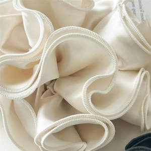 Macro detail of creamy satin hair scrunchie showing rich folds and silk-like texture