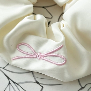 Detail of silk satin scrunchie featuring fine pink butterfly embroidery in beige color