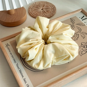 Detail of a large cream cloud scrunchie with soft pleated texture for hair styling