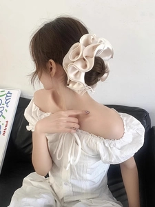 Detailed view of a champagne satin scrunchie with layered ruffles on a bun hairstyle