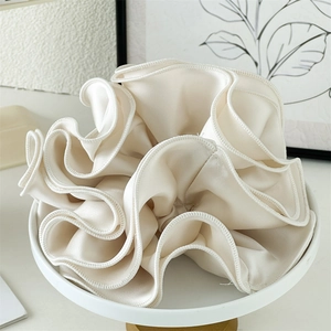 Macro detail of creamy white satin oversized scrunchie with delicate ruffled edge texture