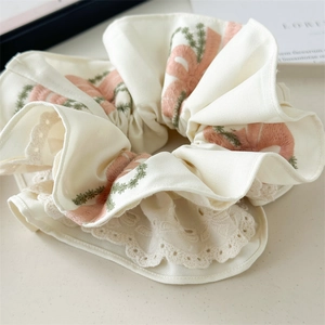 Close-up of cream-colored oversized scrunchie featuring pink floral embroidery and lace trim