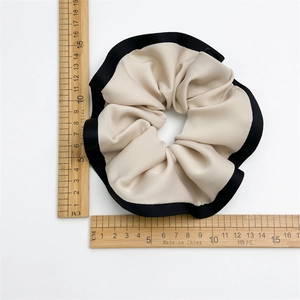 Detail showing an ivory scrunchie with black trim and measurement ruler for size reference