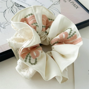 Detailed embroidery of pink bows and green vines on a beige lace scrunchie