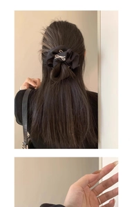 Detail view of black satin scrunchie with white bow embroidery on dark hair