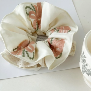 Detail of embroidered pink bows and delicate lace edges on cream cotton scrunchie
