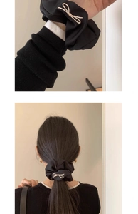 Detail view of black satin bow scrunchie showing wrist styling and elegant back hair tie