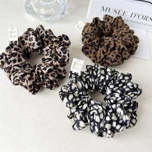 Detailed macro view of three premium leopard print satin hair scrunchies with woven labels