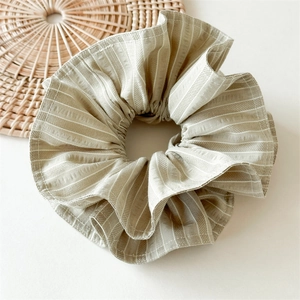 Détail macro d'un chouchou en coton beige avec de fines rayures blanches verticales