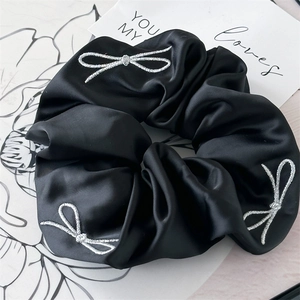 Detail of black satin scrunchie featuring elegant white bow embroidery and silk texture