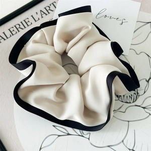 Close-up of a cream satin scrunchie with black contrast edges on a fashion magazine