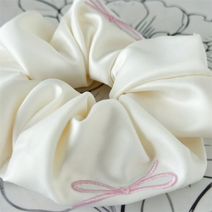 Detail of cream satin scrunchie with soft pearl luster and pink bow embroidery