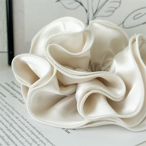 Macro shot of large cream satin scrunchie showing silky texture and ruffled edges