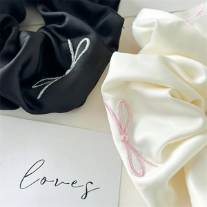 Close-up of black and cream satin hair scrunchies with delicate bow embroidery detail