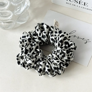 Detail of leopard print satin scrunchie with brand tag on minimalist background
