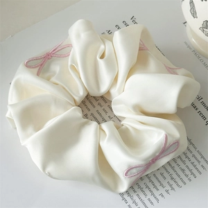 Close-up of cream satin scrunchie with pink embroidered bows on a magazine