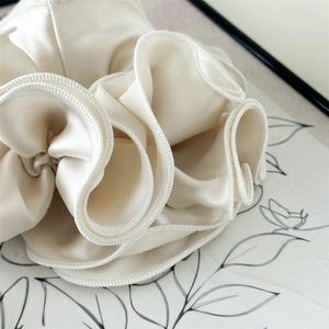 Detailed close-up of cream satin scrunchie featuring multi-layer ruffled edge and silky texture