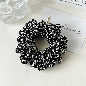 Detail of black and white leopard print scrunchie with label on minimalist background