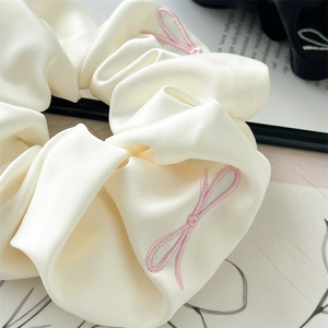 Close-up of cream and black satin scrunchies with pink bow embroidery and soft pleats