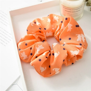 Detail of orange cat print scrunchie with polka dots on a white tray with candle décor