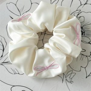 Close-up of cream satin scrunchie with delicate pink bow embroidery and silky texture